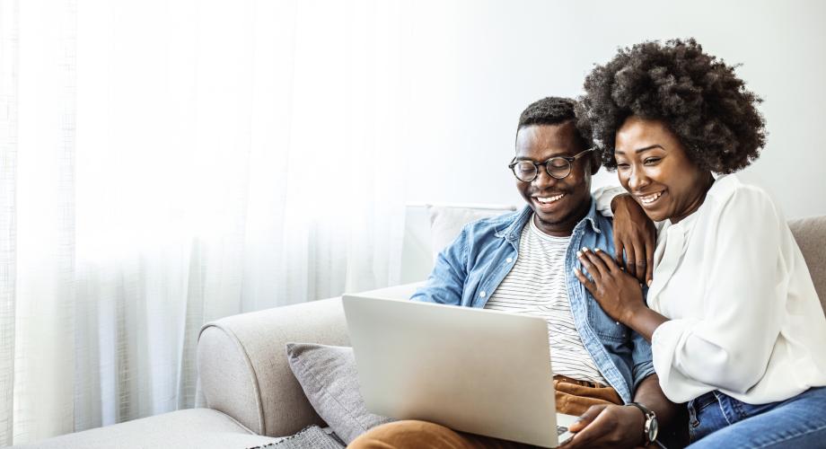 a couple sitting on the couch looking at a laptop screen and smiling