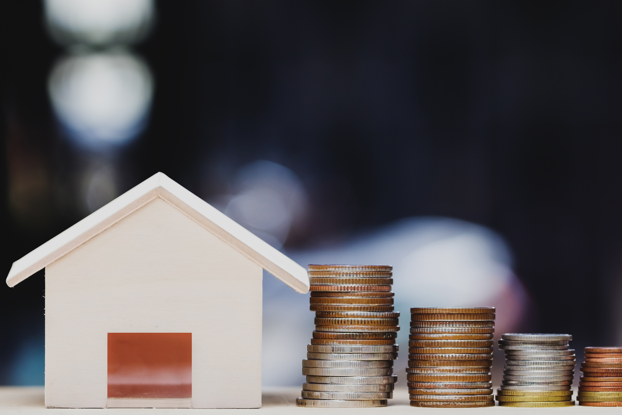 little house figurine with coins stacked next to it