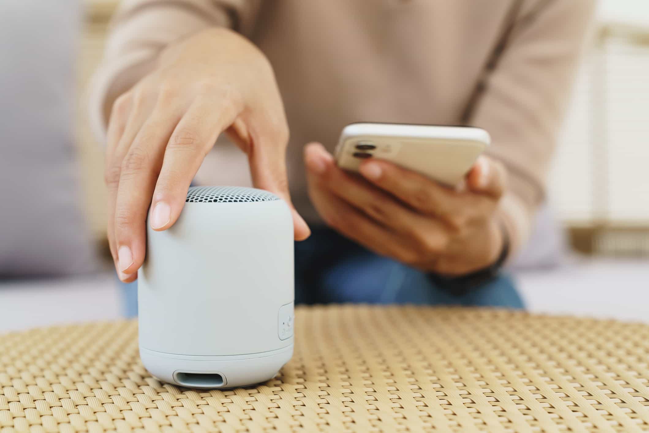 woman turning on bluetooth speaker and holding phone in other hand