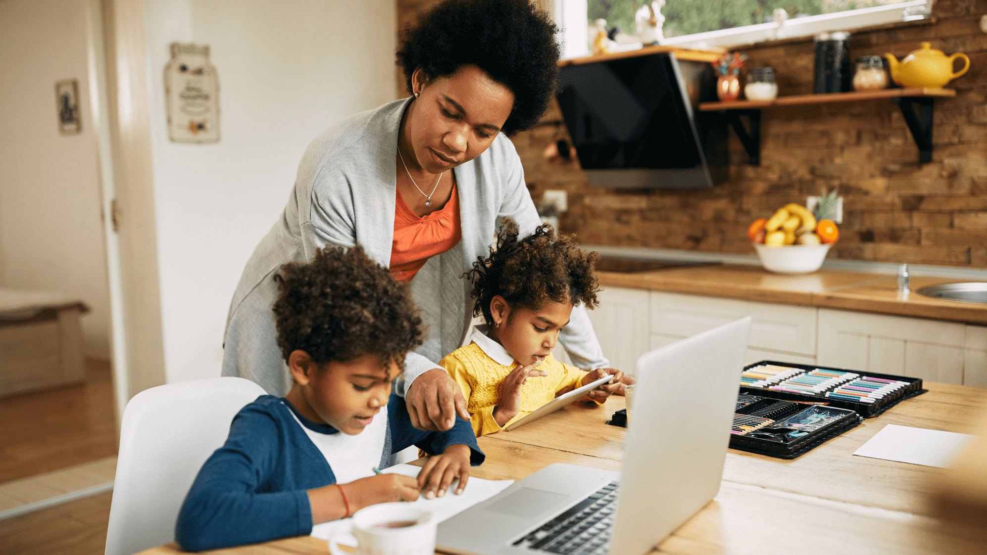 woman homeschooling young children at kitchen counter