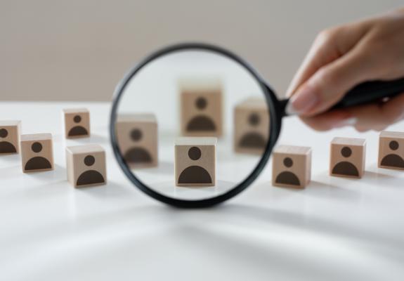 magnifying glass over little wooden headshot figurines