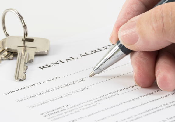 man's hand signing a rental agreement, with house keys next to it on the table