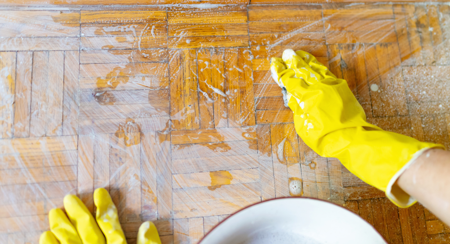 person cleaning wood floors with yellow rubber gloves on
